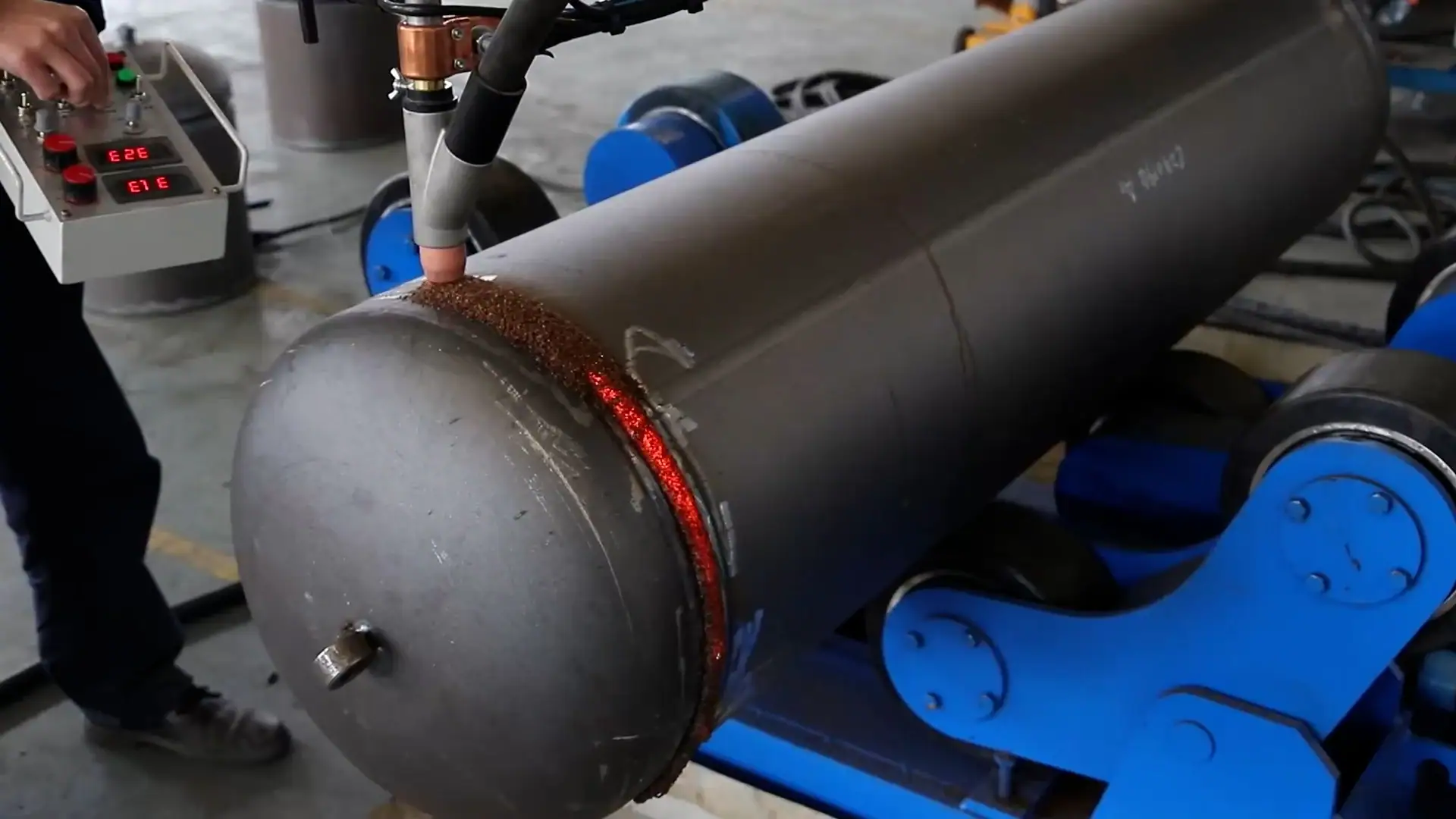 Large industrial pipe undergoing high-temperature testing or welding, with visible heat marks and welding equipment in a manufacturing or engineering facility.