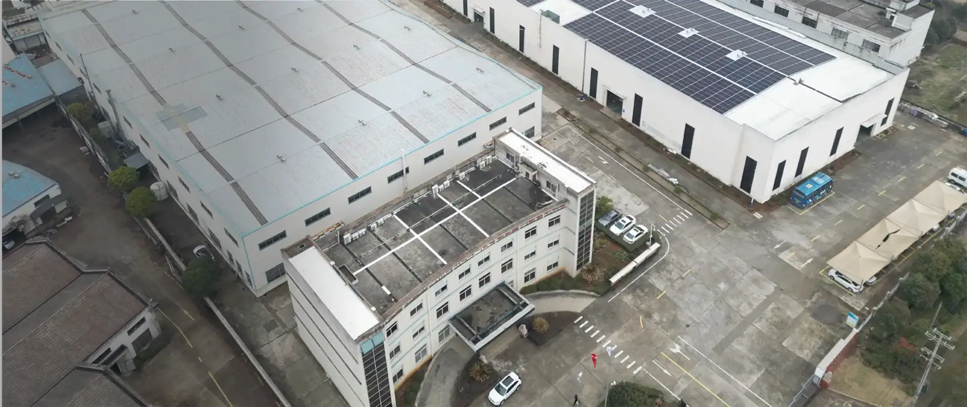 Aerial view of a large industrial warehouse featuring solar panels on the roof, surrounded by parking spaces and adjacent buildings, highlighting sustainable energy use and logistics infrastructure.